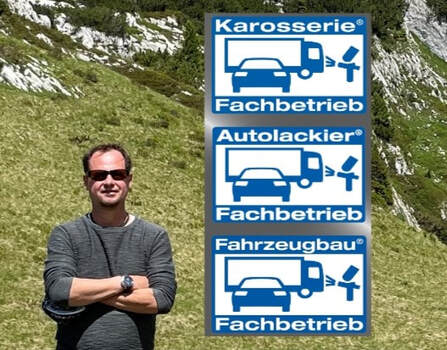 Thomas Dausinger vor den Fachbetriebskennzeichen für Karosserie, Autolackierung und Fahrzeugbau